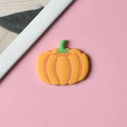 A pumpkin-shaped magnet in vibrant orange with a green stem on a pink background.