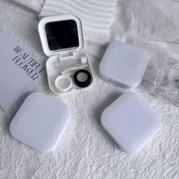 A portable contact lens case in white, featuring a mirror and compartments, displayed alongside additional cases.