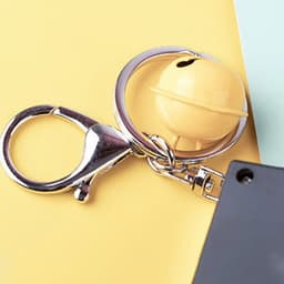 A yellow mini slot machine with a keyring attachment and a silver clasp on a pastel background.