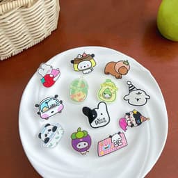 A plate displays various custom acrylic lapel pins in bright colours, featuring cute cartoon designs and a logo.