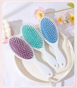 Three custom full-colour paddle hair brushes in purple, teal, and light blue, resting on a white plate with decorative items.
