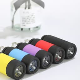 Five LED rechargeable flashlight keychains in yellow, blue, purple, red, and black, with a jar in the background.