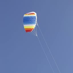 A colourful dual-line parafoil kite soaring in a clear blue sky, featuring stripes of red, yellow, green, and blue.