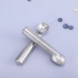 A nonstick aluminium ice cream scoop in a silver finish, placed on a light blue surface with scattered blueberries.