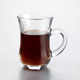 A transparent tea cup with a curved handle filled with dark liquid. The cup is made of glass and has a sleek design.
