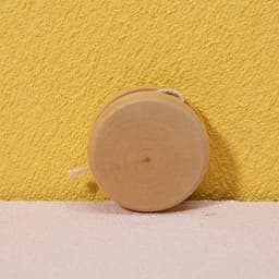 A natural wooden yoyo sits against a yellow wall, showcasing its smooth, circular design.