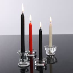 A set of four taper candles in black, red, and cream, displayed in clear glass candle holders, with flames lit.