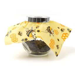 A beeswax wrap in yellow with a bee and honeycomb design covering a glass jar filled with dark contents.