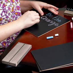 A set of tabletop chalkboard signs with a wooden base, accompanied by colourful chalk pieces, on a wooden table.