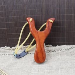 A custom wooden slingshot in a rich brown colour with yellow rubber bands and a small metal component.