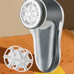 A portable lint remover in grey and white, alongside a detachable lint collector, placed on an orange fabric surface.
