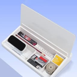 A white desktop organiser containing a ruler, markers, a USB, tape, and an eraser, with a hinged lid.