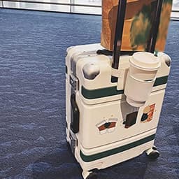 A drink bottle is securely held in a white and green luggage handle cup holder attached to a suitcase.
