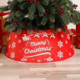 A red Christmas tree collar featuring white snowflakes and Santa’s sleigh design, positioned under a decorated tree.