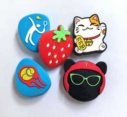 Custom tennis dampeners in various designs, featuring a strawberry, cat, tennis ball, and two playful characters, in bright colours.