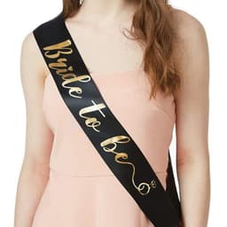 A black satin sash with gold text reading "Bride to be," worn over a pink dress.