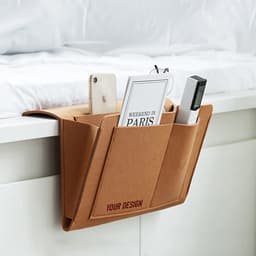 A tan felt bedside pocket with multiple compartments holding a phone, a book, and a remote control.