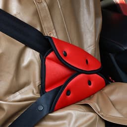 A kids car seat belt adjuster in red and black fabric, featuring buttons, placed on a car seat.