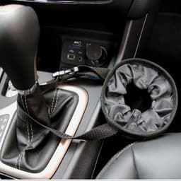 A black car seat back garbage bag with a strap, positioned beside a gear shift in a vehicle interior.