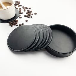 A set of black PU leather coasters with a matching holder, surrounded by coffee beans and a drink bottle.