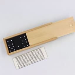 A wooden box containing a custom dominoes set with black domino pieces featuring white dots.