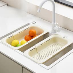 An extendable kitchen sink colander in cream colour, featuring two sections for rinsing fruits.