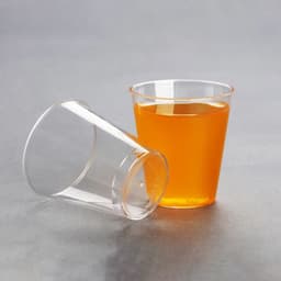 A clear plastic disposable cup with orange liquid, alongside another cup tipped over on a grey background.