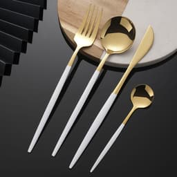 A gold and white cutlery set includes a fork, spoon, knife, and small spoon, presented on a stylish surface.