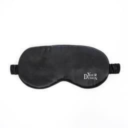 A black eye mask made of silk with elastic straps and a logo on one side.