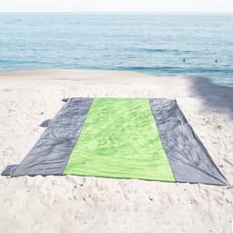 A waterproof beach picnic blanket in grey and bright green laid out on sandy beach near water.