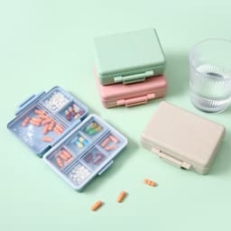 A set of custom wheat straw pill cases in green, pink, and beige, with a glass of water beside them.