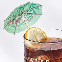 A cocktail glass topped with a green paper umbrella and a slice of lemon, featuring decorative designs.