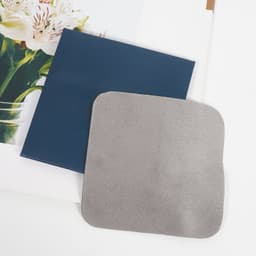 A grey microfiber eyeglasses wipe is placed on a dark blue background, alongside a floral print.