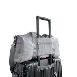 A grey large capacity duffel bag sits atop a black suitcase, featuring a handle and a zippered pocket.