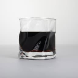 A clear, irregular whiskey glass filled with dark liquid, featuring a sleek, wavy design.