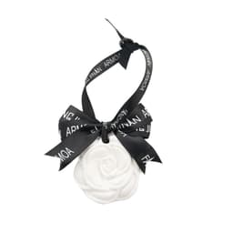 A white hanging aromatherapy tablet in the shape of a flower, tied with a black ribbon. Features a logo on the ribbon.