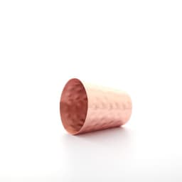 A hammered copper shot glass with a shiny finish, featuring a textured surface and a rounded shape.