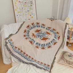 A knitted throw blanket with tassels in beige, blue, and rust colours, featuring a circular pattern.