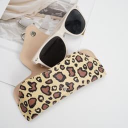 A portable glasses pouch in a leopard print design, holding a pair of black sunglasses. It features a carabiner attachment.
