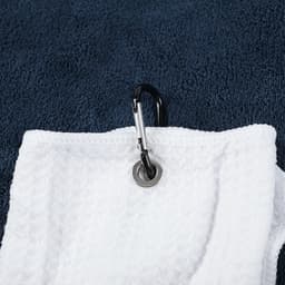 A white golf towel featuring a zippered pocket and a metal carabiner for attachment, set against a navy background.