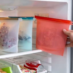 A food grade silicone storage bag in red, alongside blue and transparent bags, inside a refrigerator.
