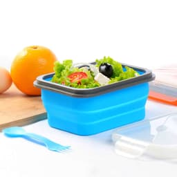 A blue collapsible lunch box with tableware, filled with salad and surrounded by fresh ingredients like an orange and eggs.