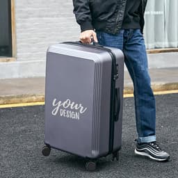 A grey 20-inch carry-on luggage with a simple design is being held by a person on a street.