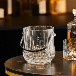 Acrylic crystal ice bucket with a handle in clear colour, featuring a decorative design, placed on a table.