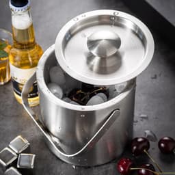 A stainless steel ice bucket with a lid and handle, holding ice and cherries, alongside a beer bottle.