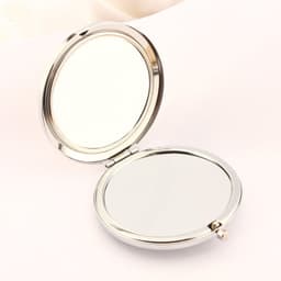 A round, double-sided makeup mirror with a shiny silver finish, opened to display both reflective surfaces.