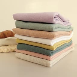 A stack of assorted linen cotton tea towels in pastel colours including pink, green, yellow, and white.