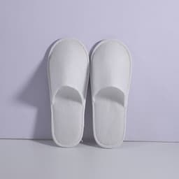 White anti-slip cloth hotel slippers displayed against a light purple background. The slippers have an open-toe design.