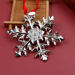 A silver metal snowflake charm adorned with rhinestones and a red ribbon for hanging.