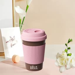 A pink and brown eco-friendly coffee mug with a ribbed sleeve and a lid, placed on a light background with flowers.